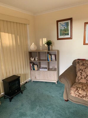 A living room with a beige sofa, a wooden bookshelf, a small black heater, and two framed pictures on the wall. - Little Hartley Hideaway (Little Hartley)