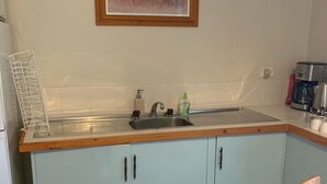 Eine Küche mit Spüle, Wasserhahn und Kaffeemaschine. Darüber hängt ein Bild an der Wand.