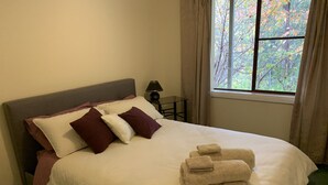 Ein ordentlich bezogenes Bett mit weißer Daunendecke, mehreren Kissen in Brauntönen und Weiß, und gefalteten Handtüchern auf dem Bett.