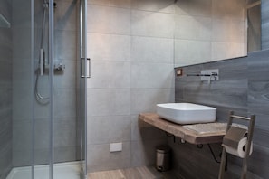 A modern bathroom with a glass shower enclosure, a white sink on a wooden countertop, and a towel rack.