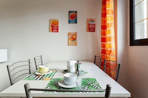 Une table à manger avec des chaises, une machine à café et un bol posé sur des sets de table.