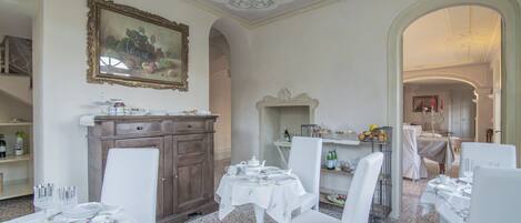 A dining area with white tables and chairs, a wooden cabinet, and a painting on the wall.