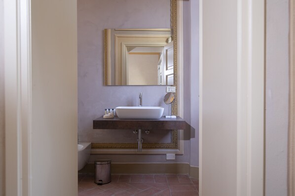 Un baño con lavamanos blanco, espejo y cubo de basura.
