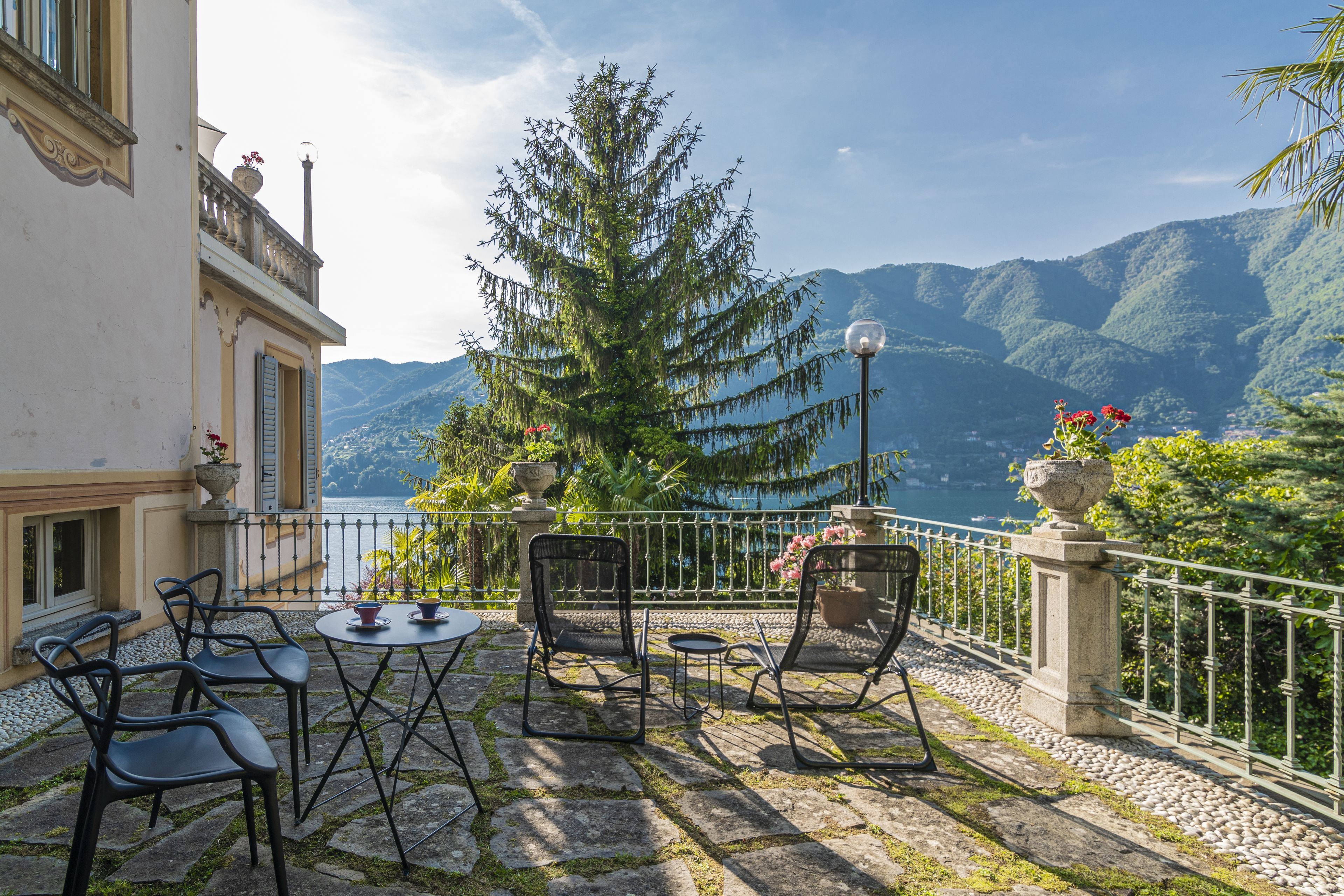 Una terraza con mobiliario exterior, vista al lago y montañas al fondo.