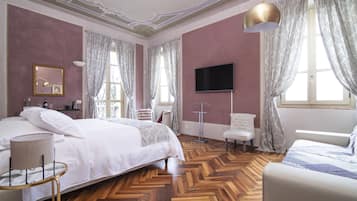 A bedroom with a large bed, a TV, a chair, and a desk with a lamp.