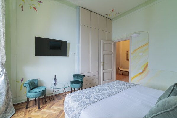 A bedroom with a bed, two chairs, a small table, and a TV mounted on the wall.