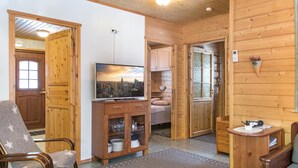 Ein gemütliches Blockhaus-Interieur mit Holzausstattung, einem Fernseher auf einem Holzschrank, einem Essbereich und einer kleinen Küche.
