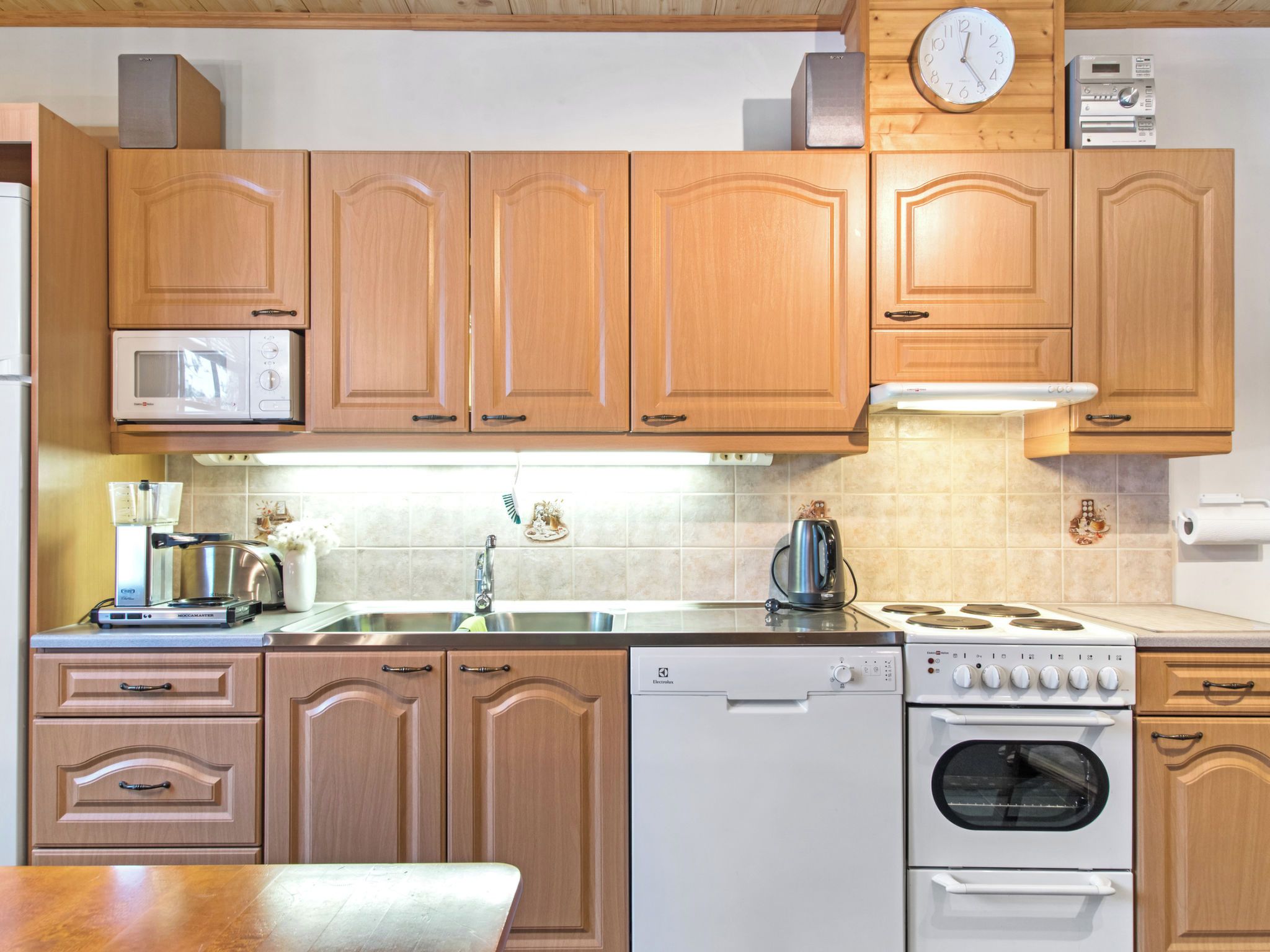 A kitchen with wooden cabinets, a microwave, a dishwasher, a stove, and a clock.