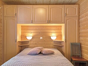A wooden cabin room with a bed, two bedside tables, and a chair. - Kurunkynsi ii by Interhome (Äkäslompolo)