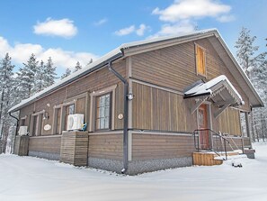 A wooden cabin with a covered porch and a chimney, surrounded by snow-covered trees. - Kurunkynsi ii by Interhome (Äkäslompolo)