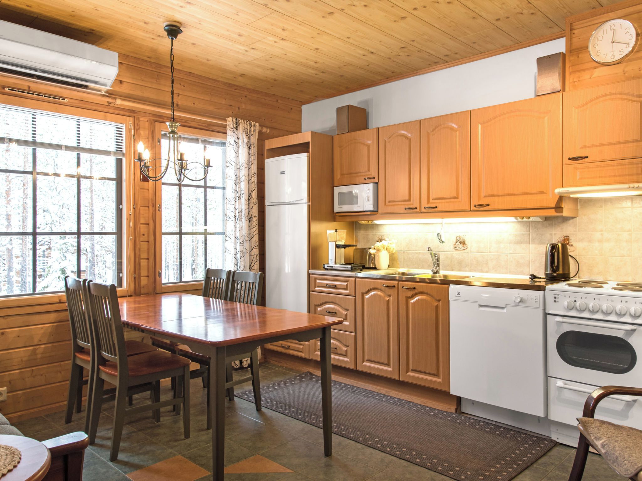 A kitchen with wooden cabinets, a refrigerator, microwave, stove, and a dining table with chairs.