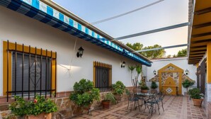 A courtyard with a tiled floor, potted plants, outdoor furniture, and a stone wall. - Villa San Vicente by Interhome (Córdoba/Baena)