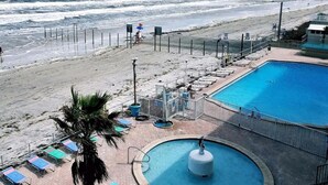 Zona de piscina frente a la playa, con vista al océano, una palmera y sillas de descanso.
