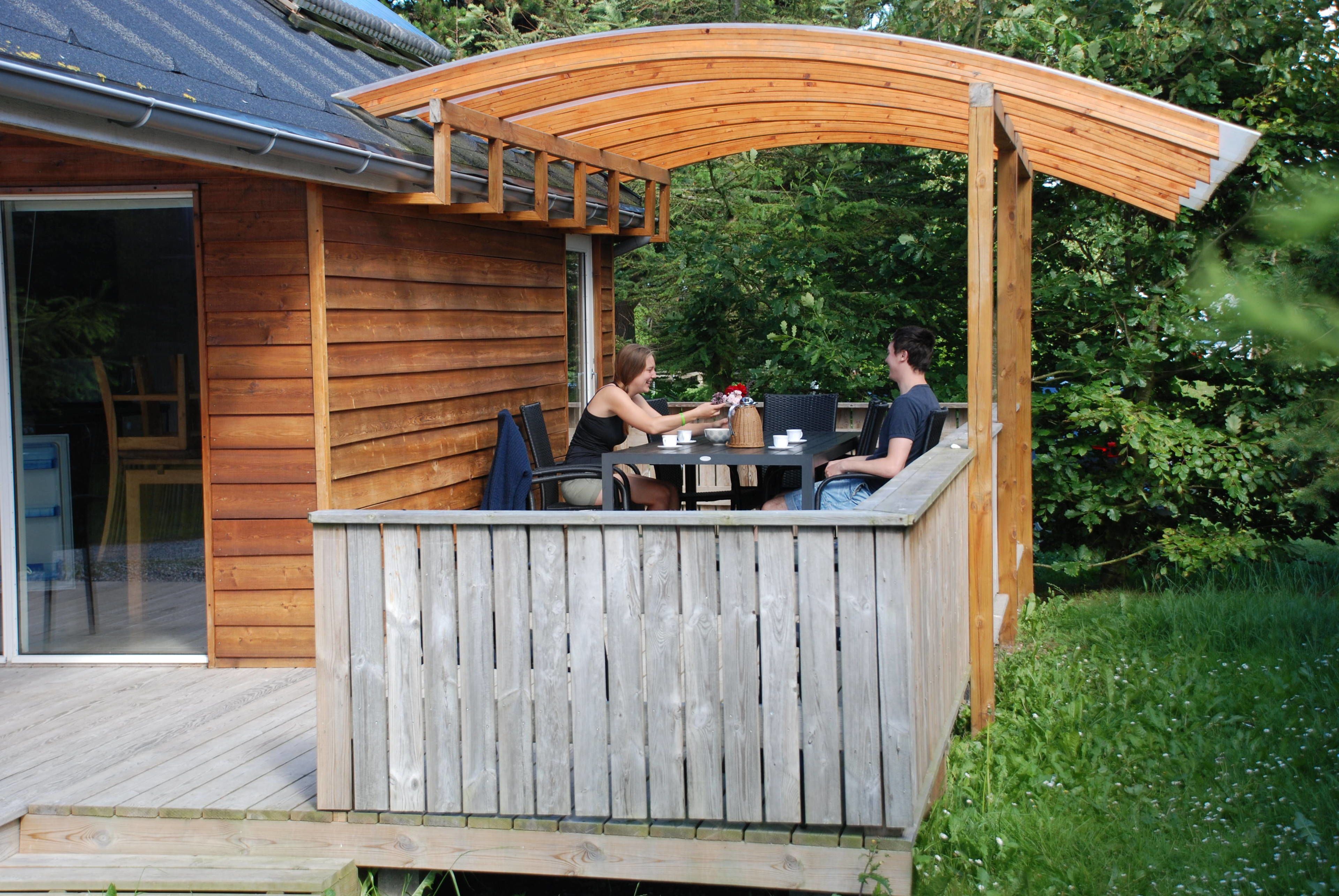 A wooden deck with a covered seating area, a table, and chairs.