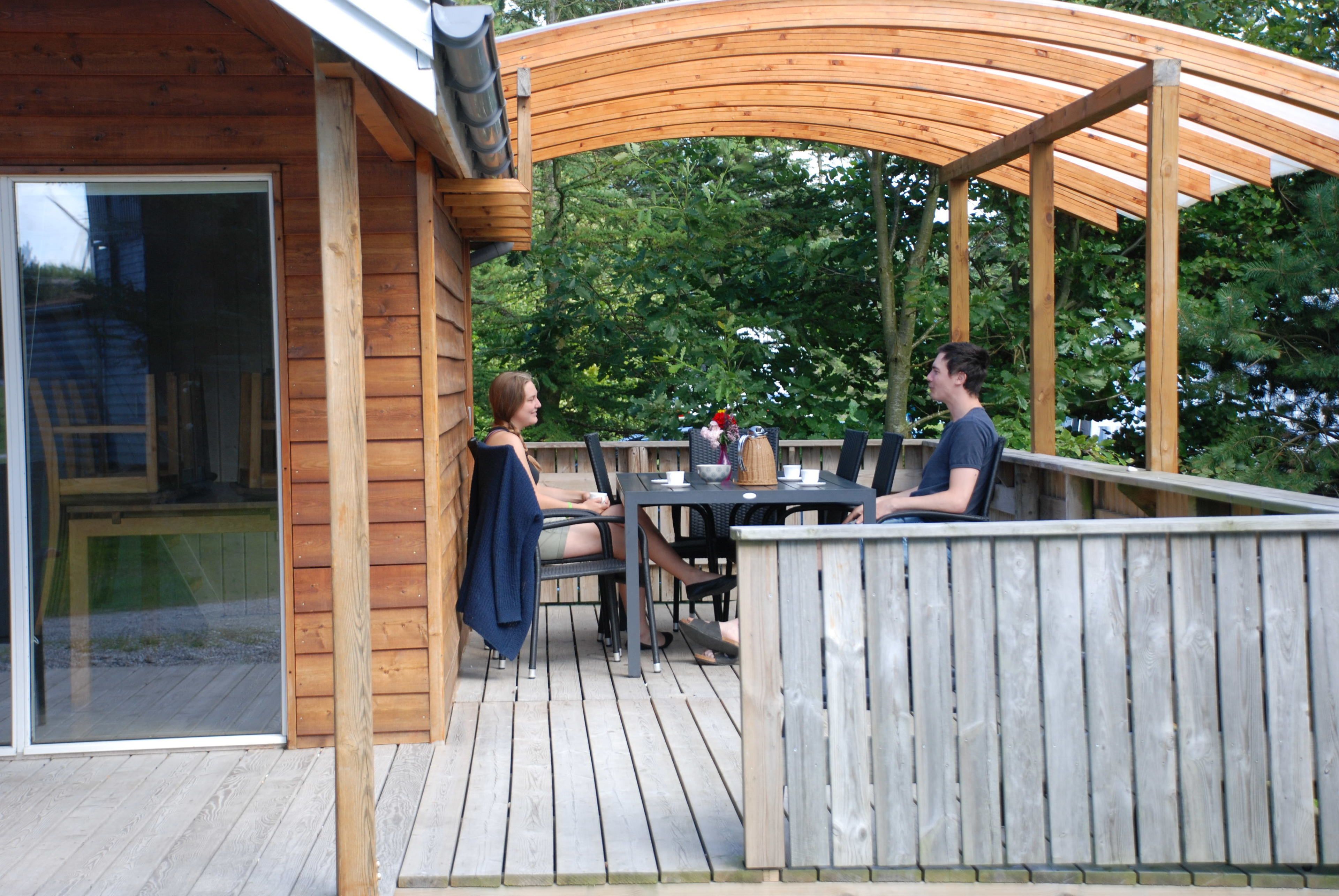 Una terraza de madera con un espacio de estar cubierto, una mesa y sillas.