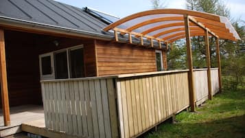 A wooden cabin with a covered deck and a large window.