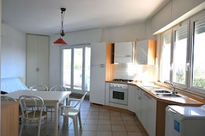 A compact kitchen with a dining area, a stove, a sink, and a window providing natural light. - M006 - Marcelli, new three-room apartment 50 meters from the sea (Marcelli)
