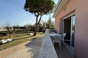 Een balkon met een tafel en stoelen, een boom en een gebouw met een schuifdeur van glas.