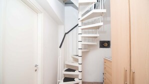 A white spiral staircase in a narrow hallway with a wooden cabinet and a door on the left.