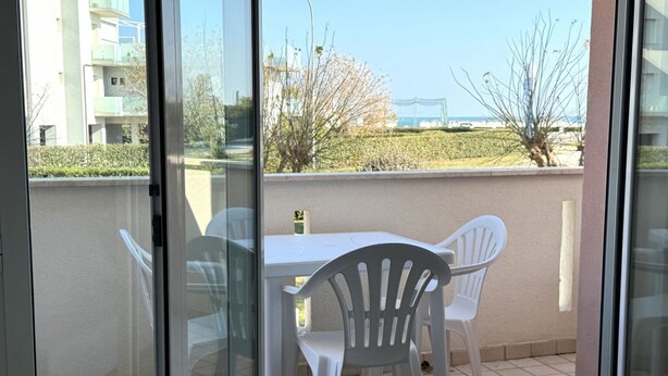 A balcony with a table and chairs, a view of a building, and a tree.