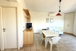 Een kamer met een houten bureau, een televisie, een eettafel met stoelen, een bed en een kledingkast.