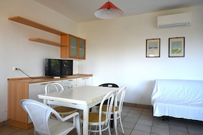 A small kitchenette with a TV, a dining table with chairs, a sofa, and two framed pictures on the wall. - M006 - Marcelli, new three-room apartment 50 meters from the sea (Marcelli)