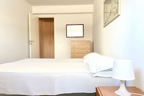 Een slaapkamer met een bed, nachtkastje, lamp, kapstok en een deur.