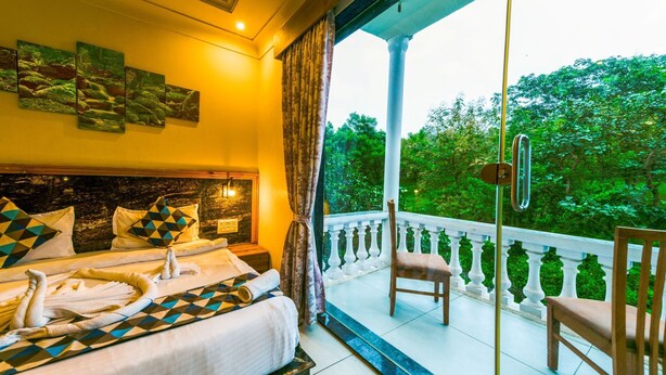 A bedroom with a bed, a chair, and a balcony with a railing. - Van Vihar Farm & Resort (Talala)