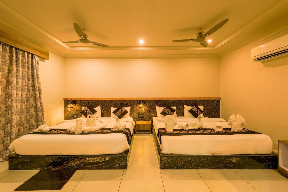 A hotel room with two beds, ceiling fans, an air conditioning unit, and a decorative wall panel.