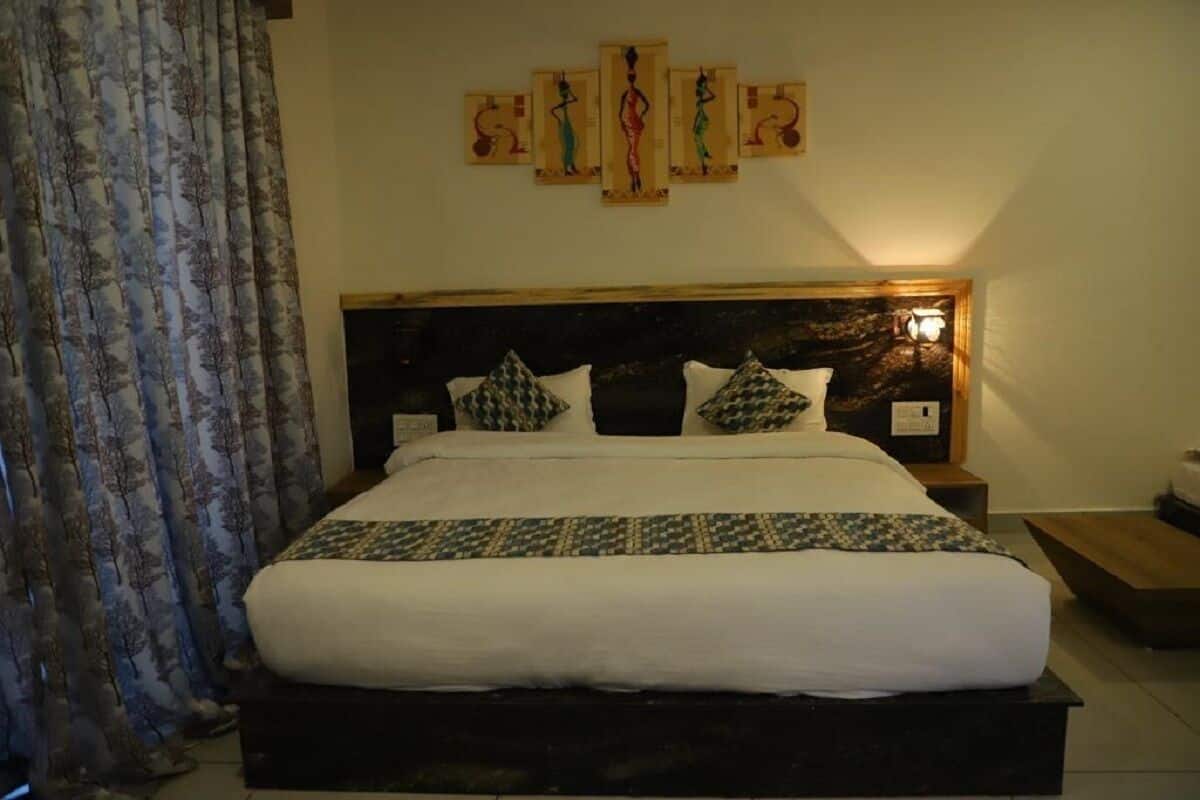 A neatly made bed with a patterned bedspread, a headboard with a light fixture, and a wall art piece above it.