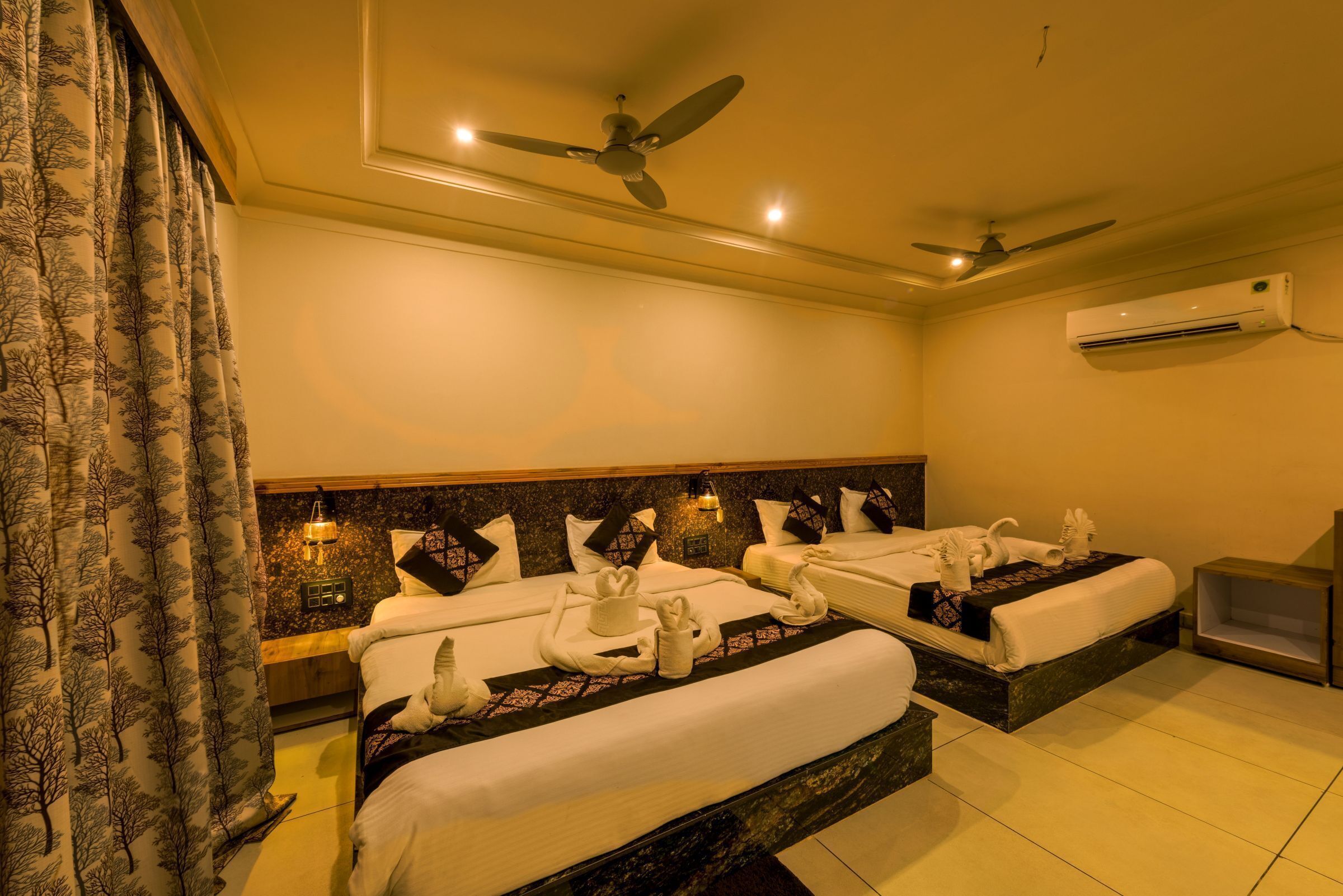 A hotel room with two beds, a ceiling fan, an air conditioning unit, and a nightstand with a lamp.
