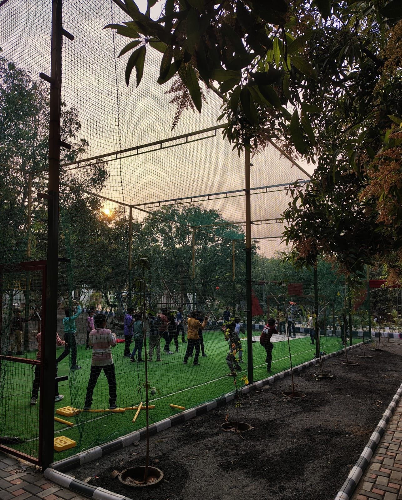 An outdoor sports facility with a netted area for activities, surrounded by trees and a green field.