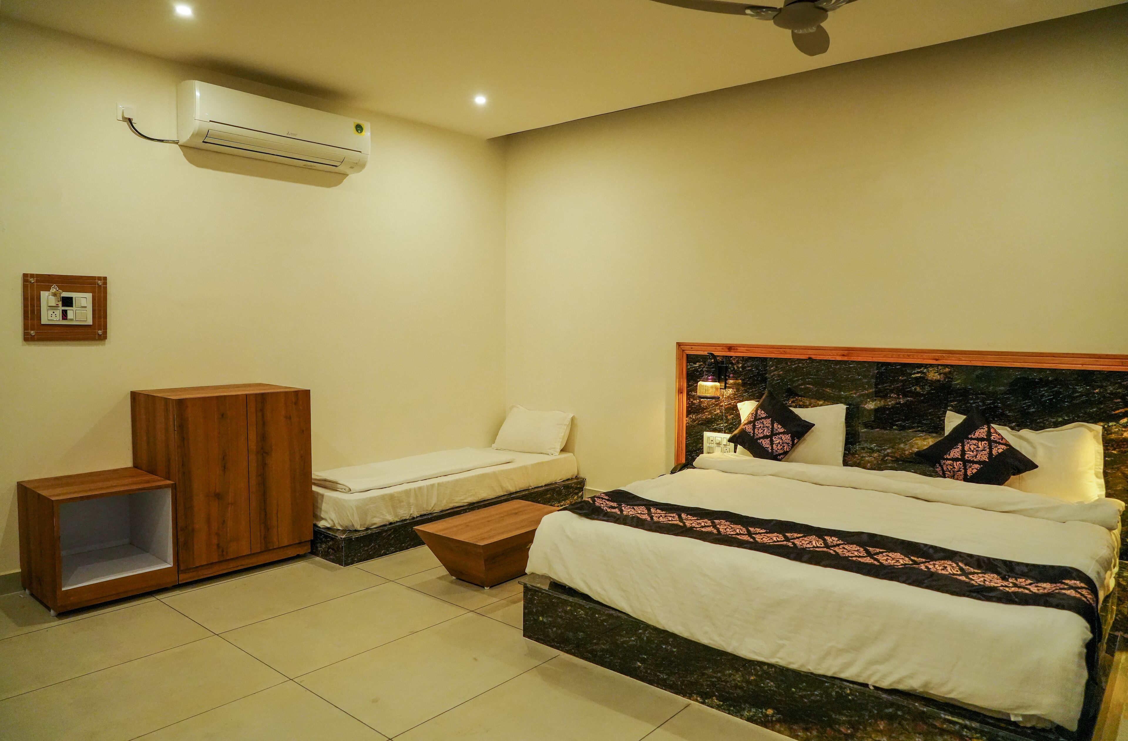 A bedroom with a bed, a wooden cabinet, a small table, and an air conditioning unit.