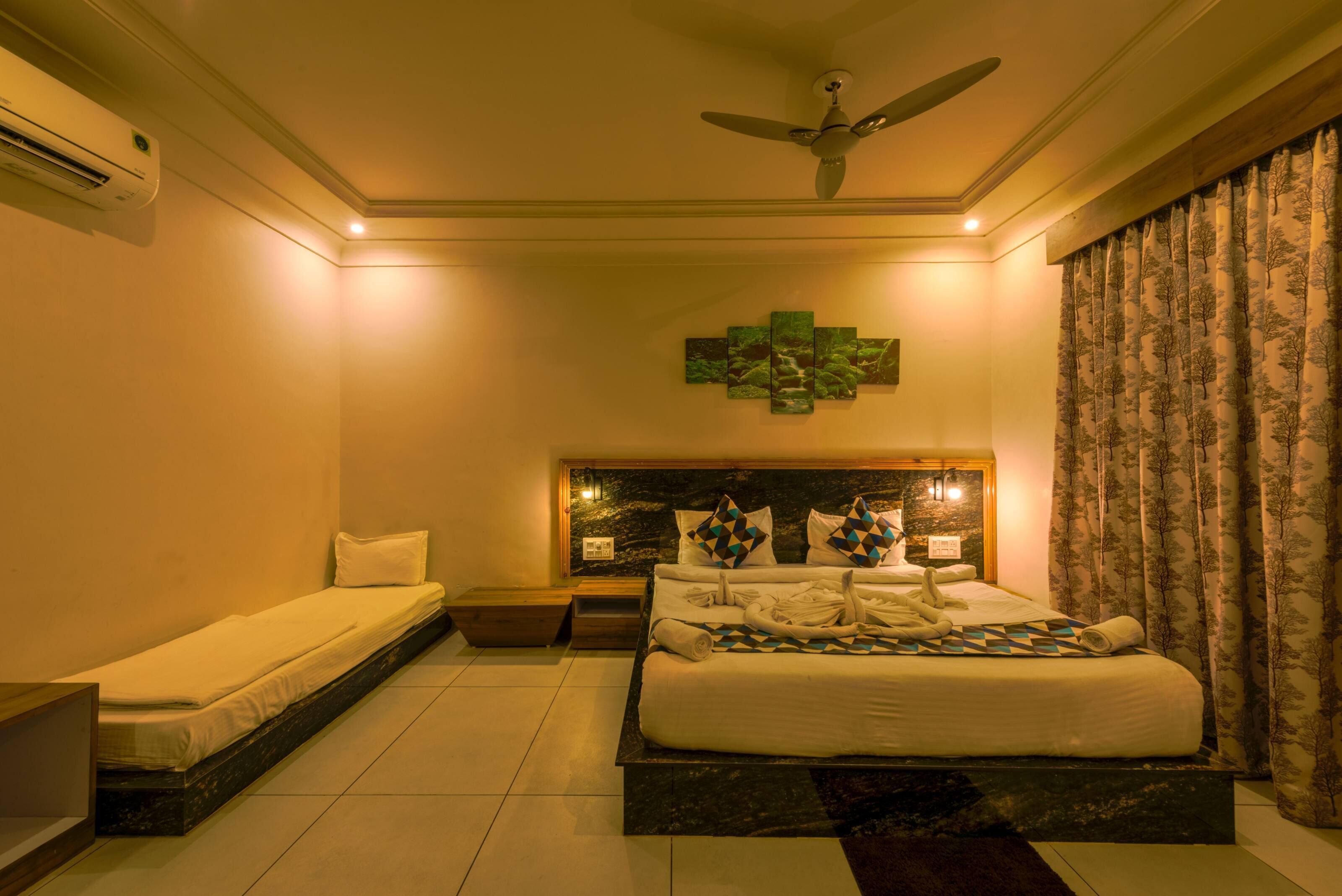 Una habitación de hotel con cama, mesita de noche, ventilador de techo y una obra de arte en la pared.