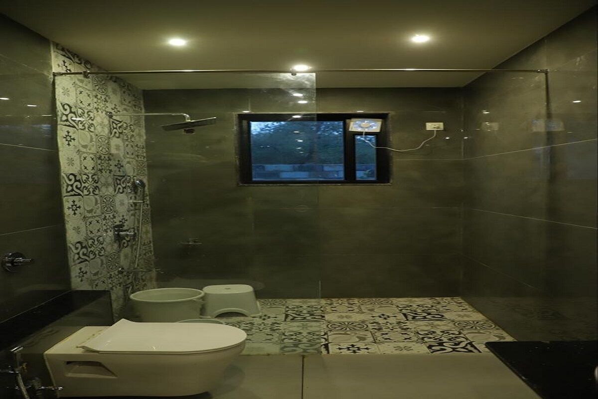 A modern bathroom with a shower, toilet, and bidet. It features a window with a view of trees and a tiled floor with a geometric pattern.