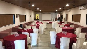 A conference room with round tables, white chairs, and red tablecloths. - Van Vihar Farm & Resort (Talala)