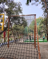 Un parque infantil con una estructura de escalada con red, rodeado de árboles y una zona pavimentada.