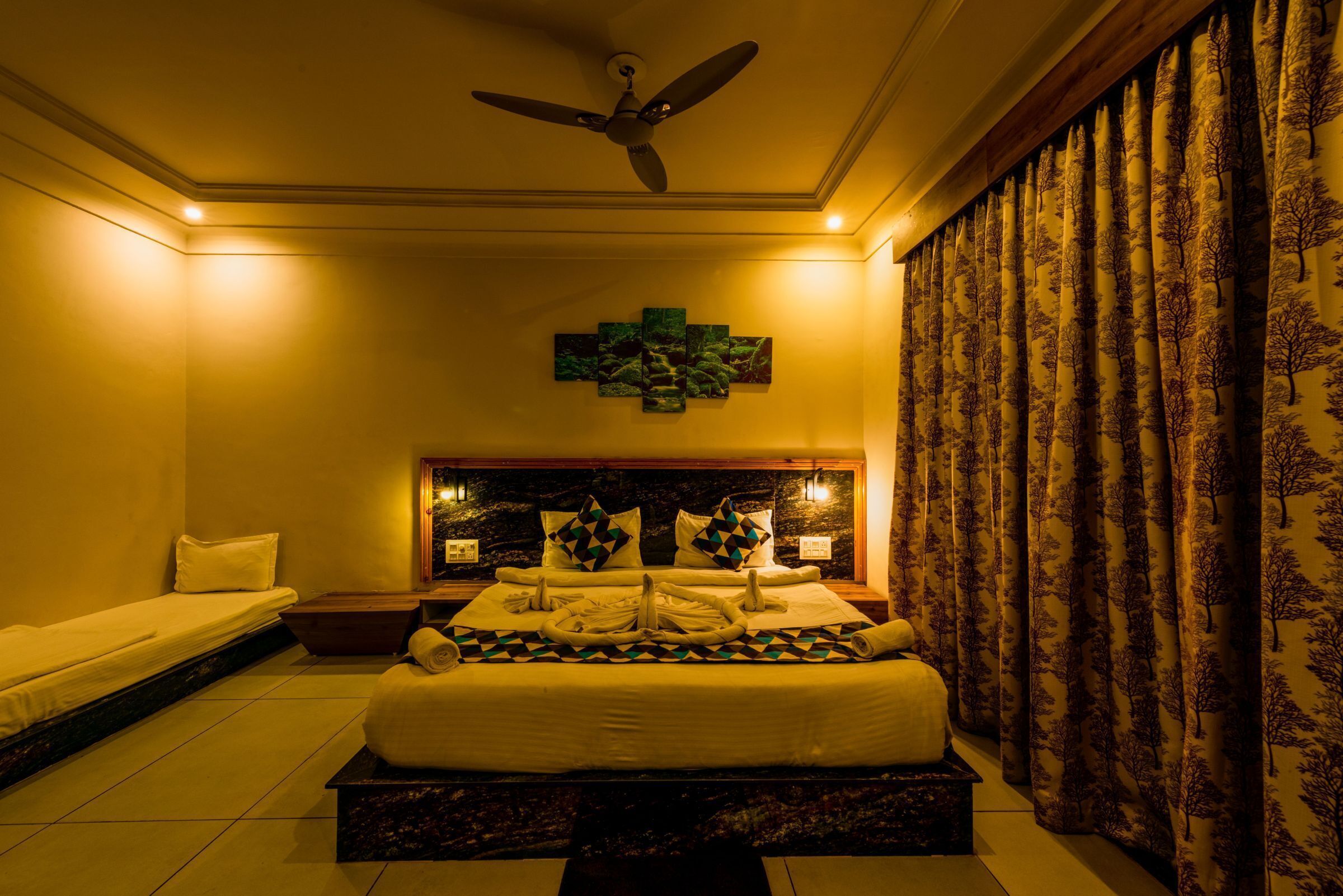 A hotel room with a large bed, a ceiling fan, a decorative wall piece, and patterned curtains.