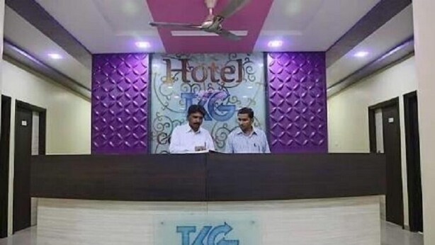 A reception desk with a logo and two staff members. - Iroomz VKG Complex (Bijapur)