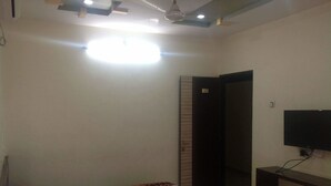 A hotel room with a bed, a TV mounted on the wall, and a door leading to another room. - Iroomz VKG Complex (Bijapur)