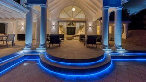 Ein überdachter Außenbereich mit Säulen, einer zentralen Sitzgruppe und blauer LED-Beleuchtung an den Stufen.