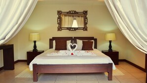 Una camera d'albergo con un letto grande, due comodini con lampade, uno specchio a parete e tende bianche.