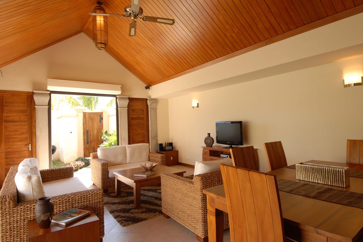 Amplia sala de estar con techo de madera, televisor y una mesa de comedor con sillas.