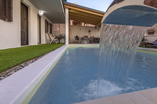 A swimming pool with a waterfall feature, surrounded by a patio area with outdoor furniture.