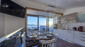 A modern dining area with a round table, white chairs, and a view of the sea through large windows. - Perfectly located holiday home with a private pool (Stanici, Omiš)