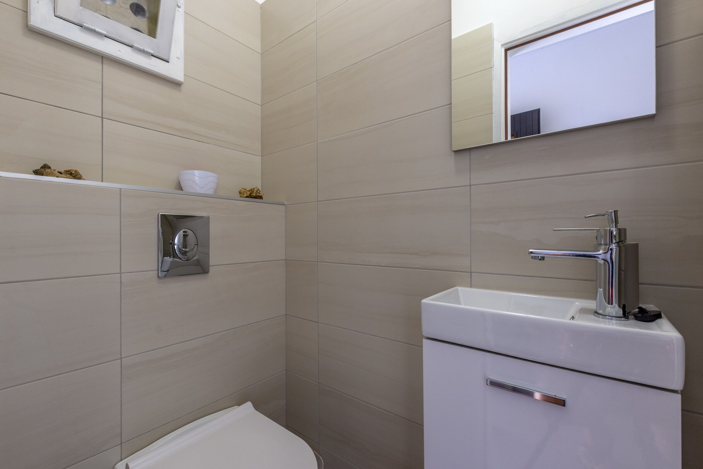 Een moderne badkamer met toilet, een wastafel met chromen kraan en een spiegel boven de wastafel.