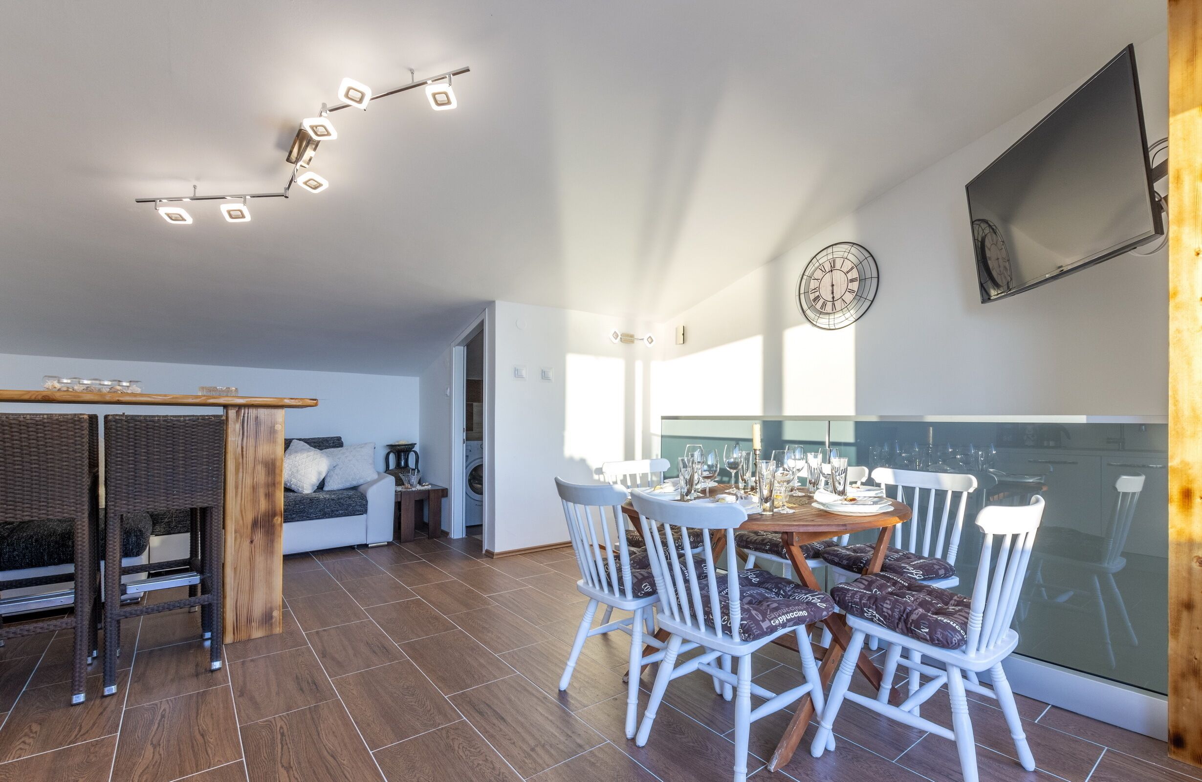 A modern kitchen with a dining area, featuring a wooden table, white chairs, and a large window.
