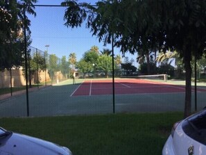 Een tennisbaan met een net, omringd door een hek en bomen.