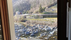A window with a view of a rocky stream and a park with a statue. - VALLEY OF GRESSONEY FONTAINEMORE TRILOCALE (Fontainemore)