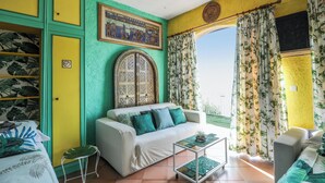 A room with a white sofa, green cushions, a small table, and a large window with curtains. - Homerez - Studio in Menton (Menton)
